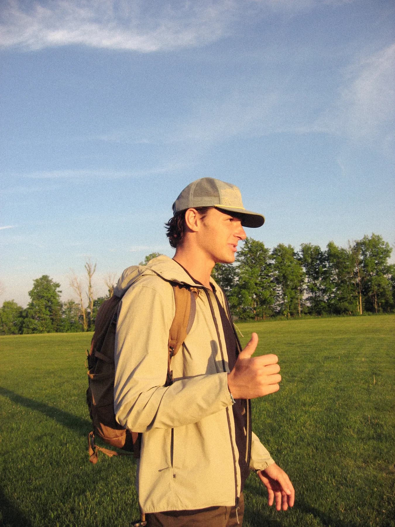 A person in a cap and backpack giving a thumbs-up in a sunlit field